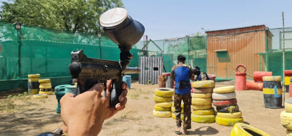 A person aims a paintball gun in an outdoor arena with other players and obstacles.