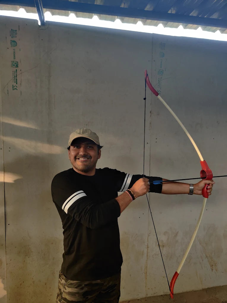 A man in a baseball cap and black shirt holds a bow and arrow, ready to shoot.