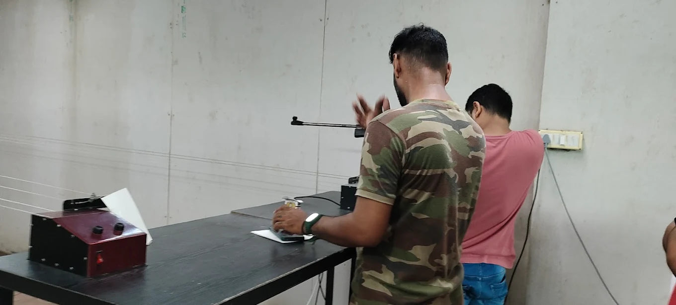 Two young men are in a room, one operating a device on a table while the other stands nearby.