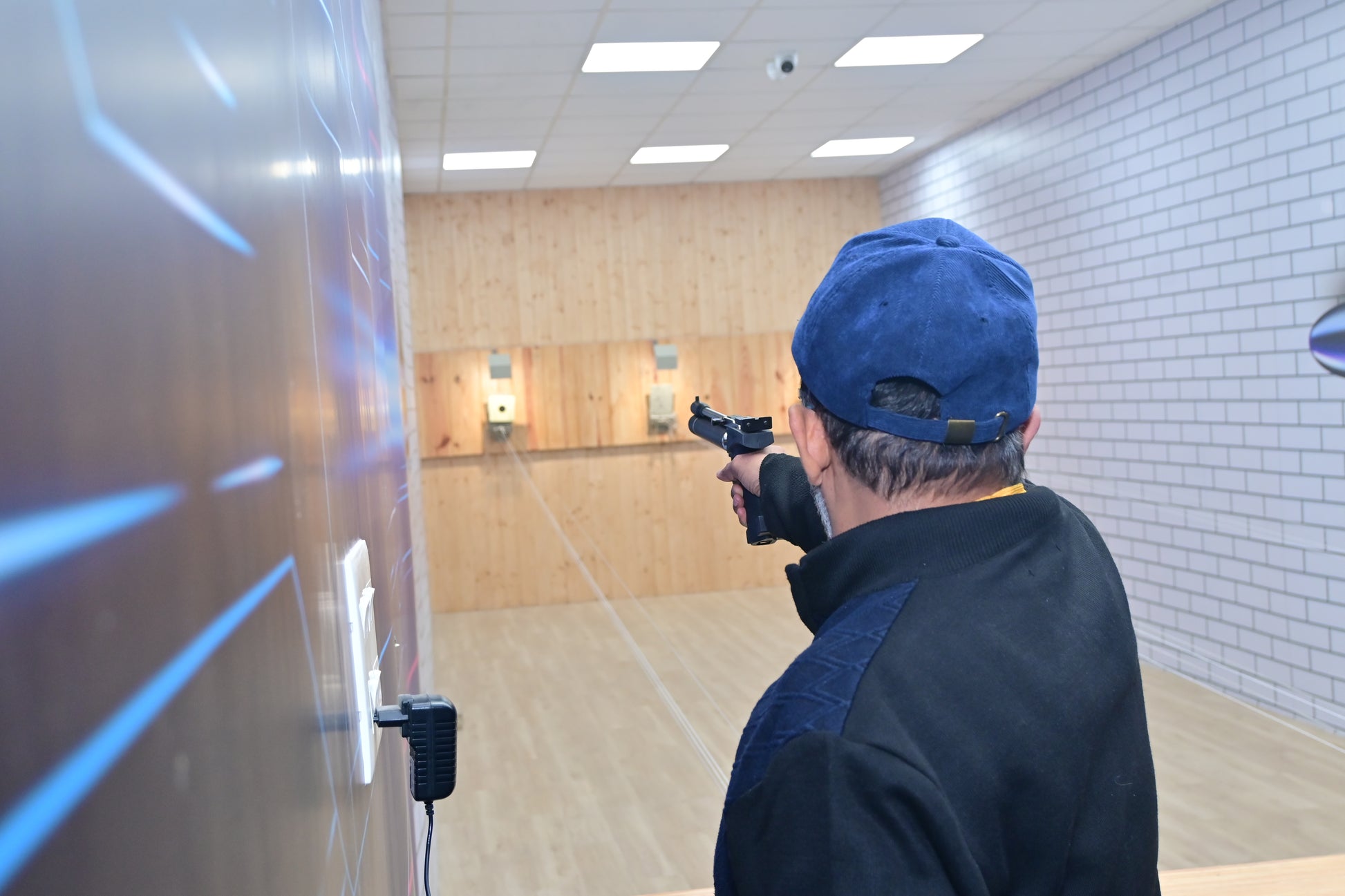 Person in a blue cap holding a gun in an indoor shooting range.
