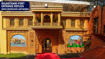 A Rajasthani fort entrance replica with intricate artwork, featuring a procession on an elephant and people walking.