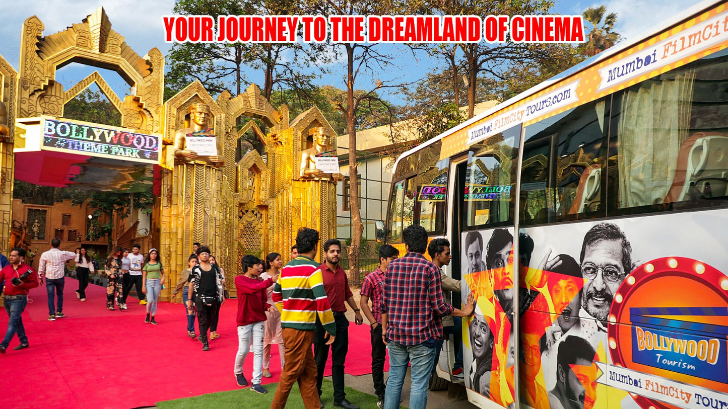 People walk on a red carpet towards a Bollywood theme park entrance, with a tour bus featuring movie stars parked nearby.