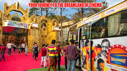 People walk on a red carpet towards a Bollywood theme park entrance, with a tour bus featuring movie stars parked nearby.