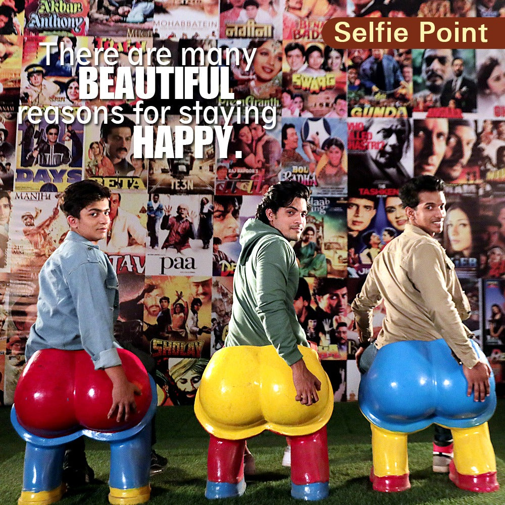 Two young men sit on novelty butt-shaped seats in front of a wall of movie posters.