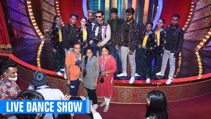 A group of young adults and children pose for a photo on a stage, some wearing sparkly outfits.