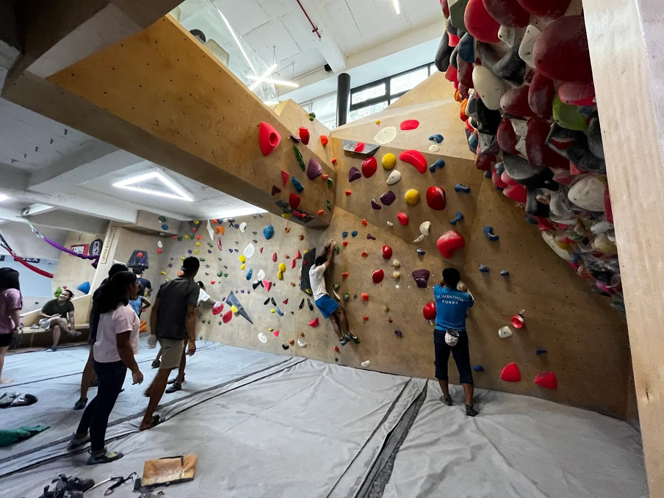 Adults boulder at an indoor climbing gym with colorful holds on a wooden wall.