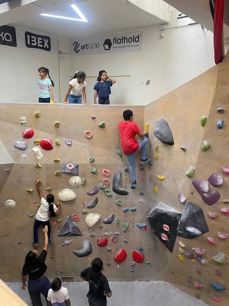 Children and young adults climb on a colorful indoor bouldering wall.