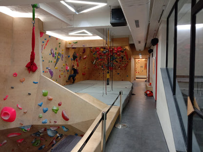 A person climbs a bouldering wall in an indoor gym with colorful holds and aerial silks.