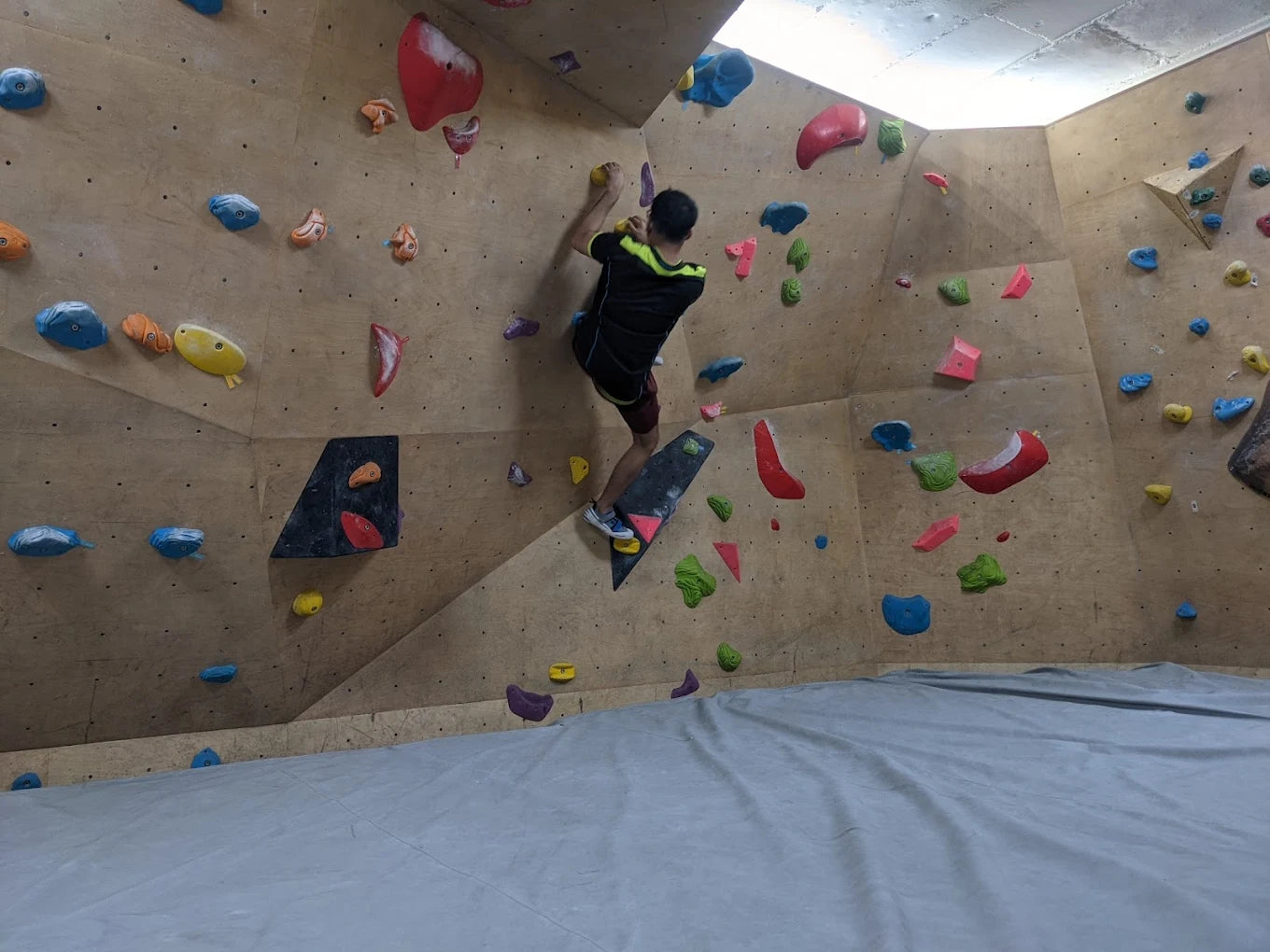 A young person bouldering on a wooden climbing wall with colorful holds.