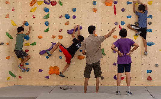 Children climbing on a colorful rock wall indoors with a safety mat below.