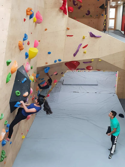 Young people climb a bouldering wall in an indoor gym.