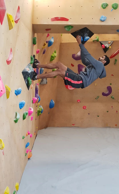 A young man bouldering on a climbing wall, reaching for a hold.