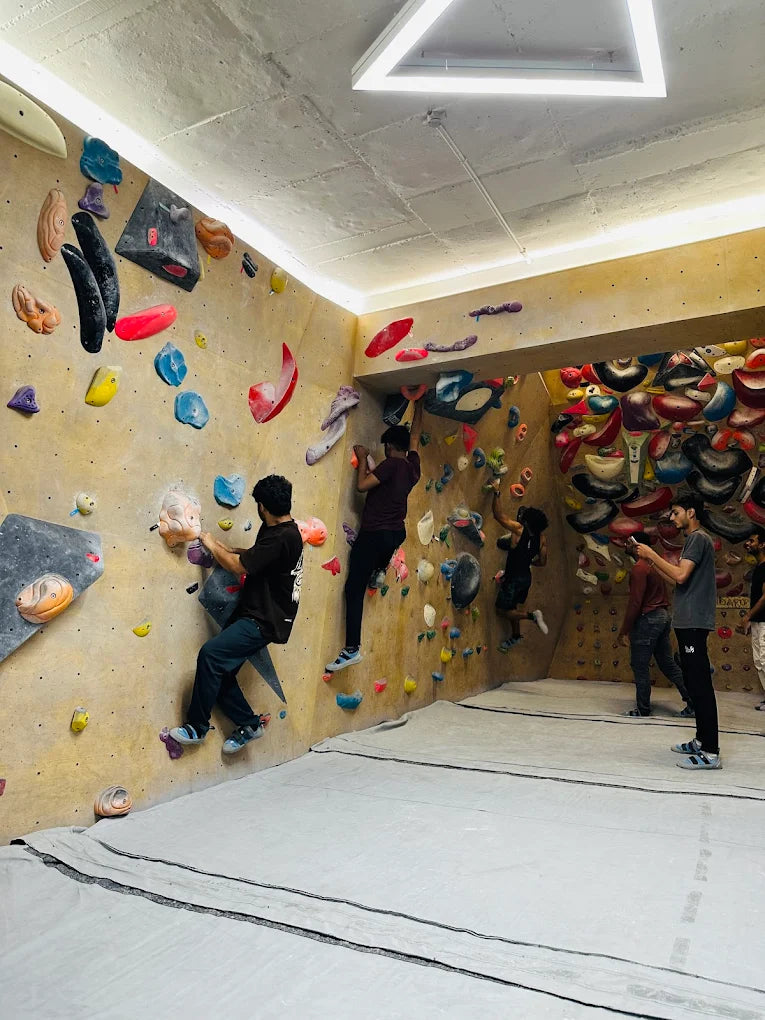 Young adults boulder on colorful climbing walls in an indoor gym.