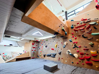 An indoor bouldering gym with colorful climbing holds on wooden walls and padded flooring.
