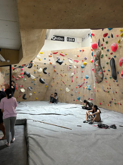 Young adults boulder in an indoor climbing gym with colorful holds on a textured wall.