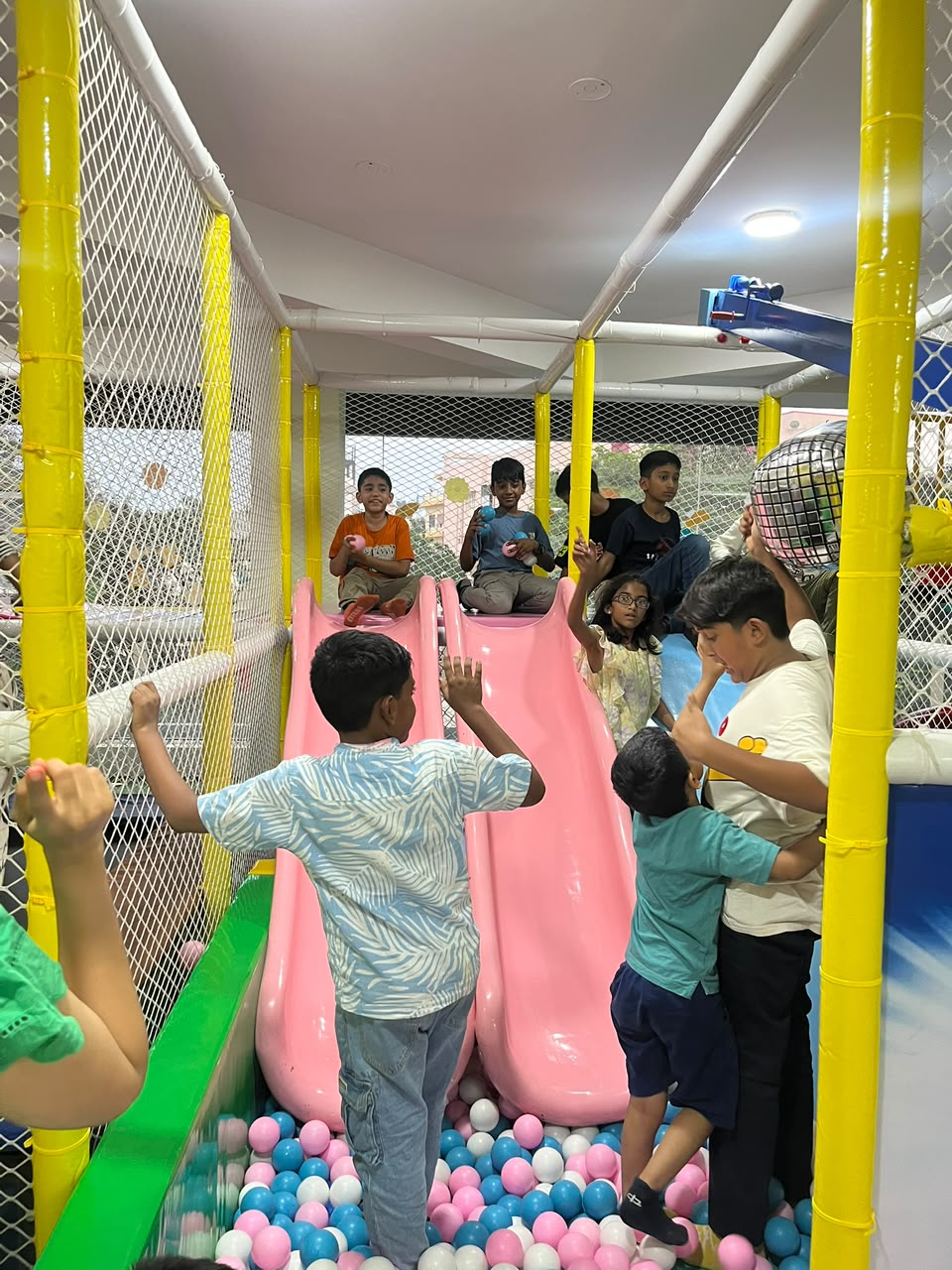 Children play in a colorful indoor playground with slides and a ball pit.