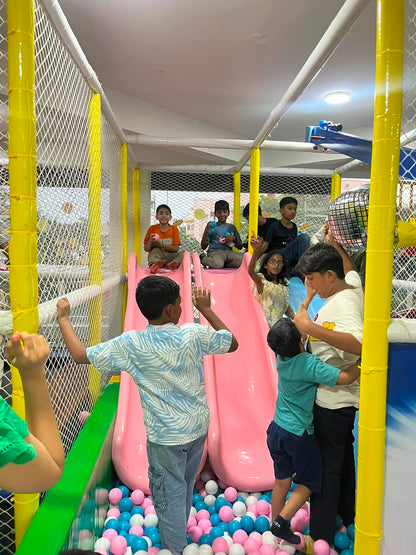 Children play in a colorful indoor playground with slides and a ball pit.