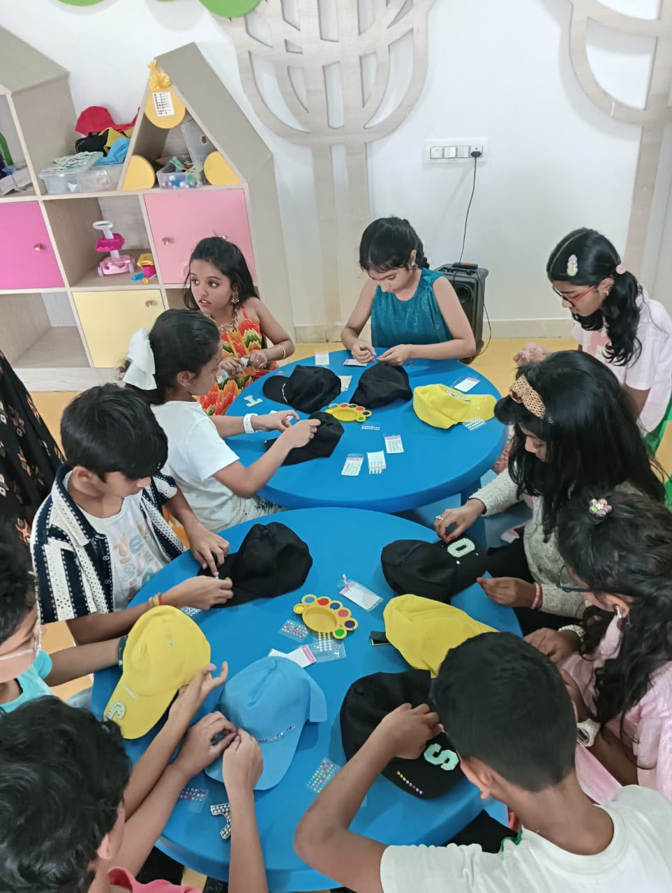 Children decorate hats at a blue table in a bright room.