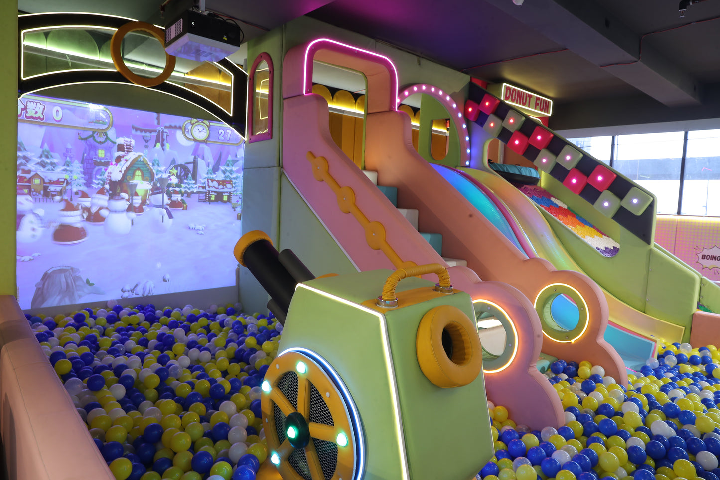 A colorful indoor playground with slides, a ball pit, and a projected winter scene, likely for young children.