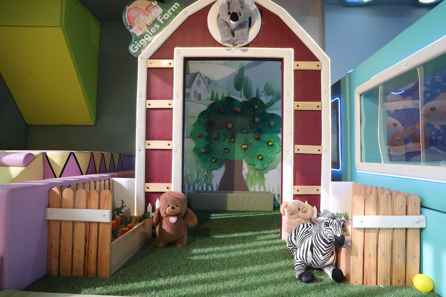 A farm-themed play area with stuffed animals, including a bear and a zebra, on artificial grass.