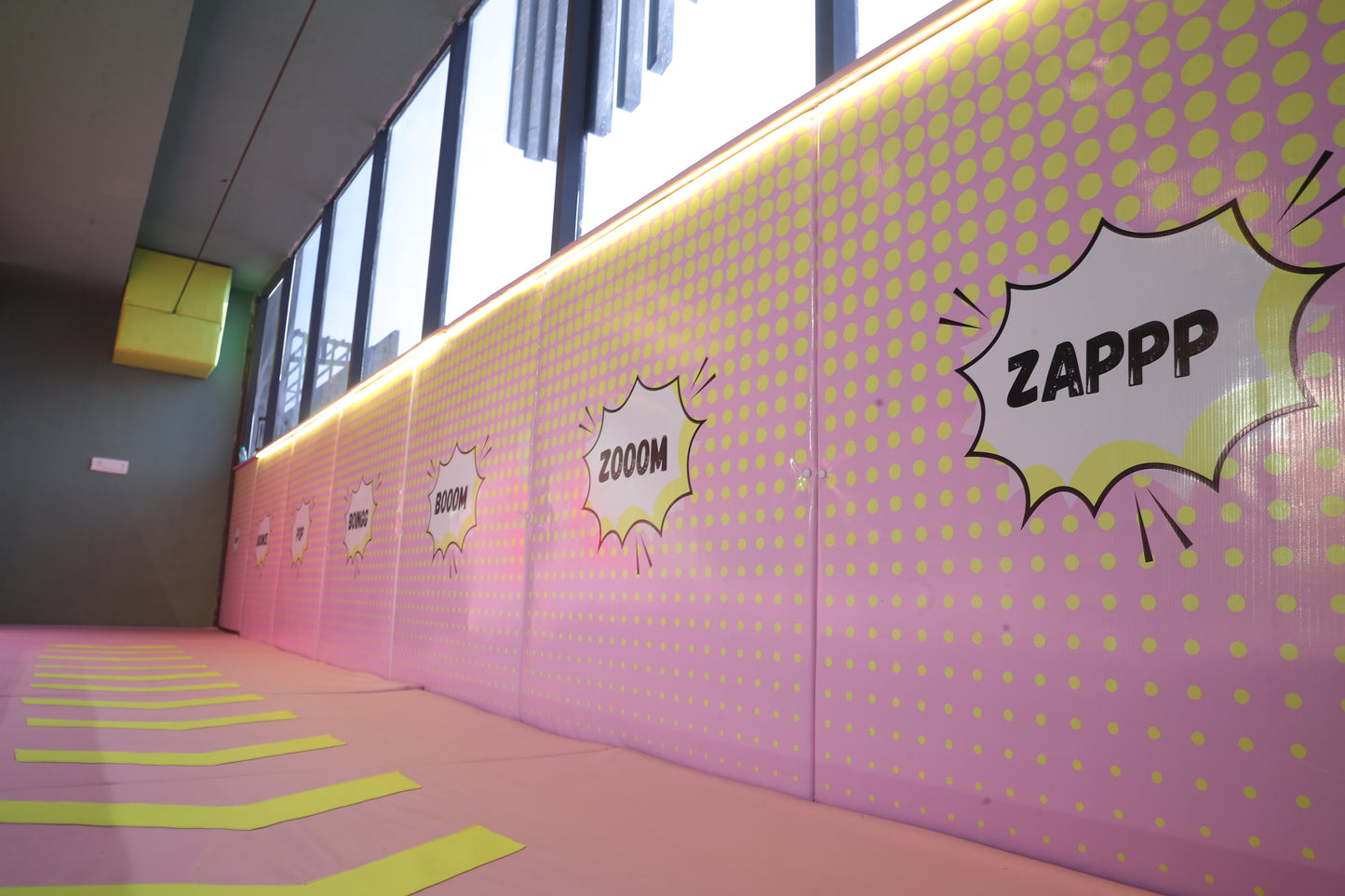 A pink wall with yellow polka dots and comic book style sound effects like "ZAPPP" and "ZOOM" is decorated with yellow lines on the floor.