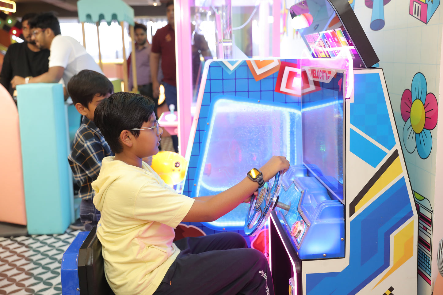 Child playing an arcade game in a colorful indoor setting with other people around.