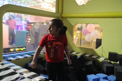 A young girl in a red shirt stands in a foam pit at an indoor playground.