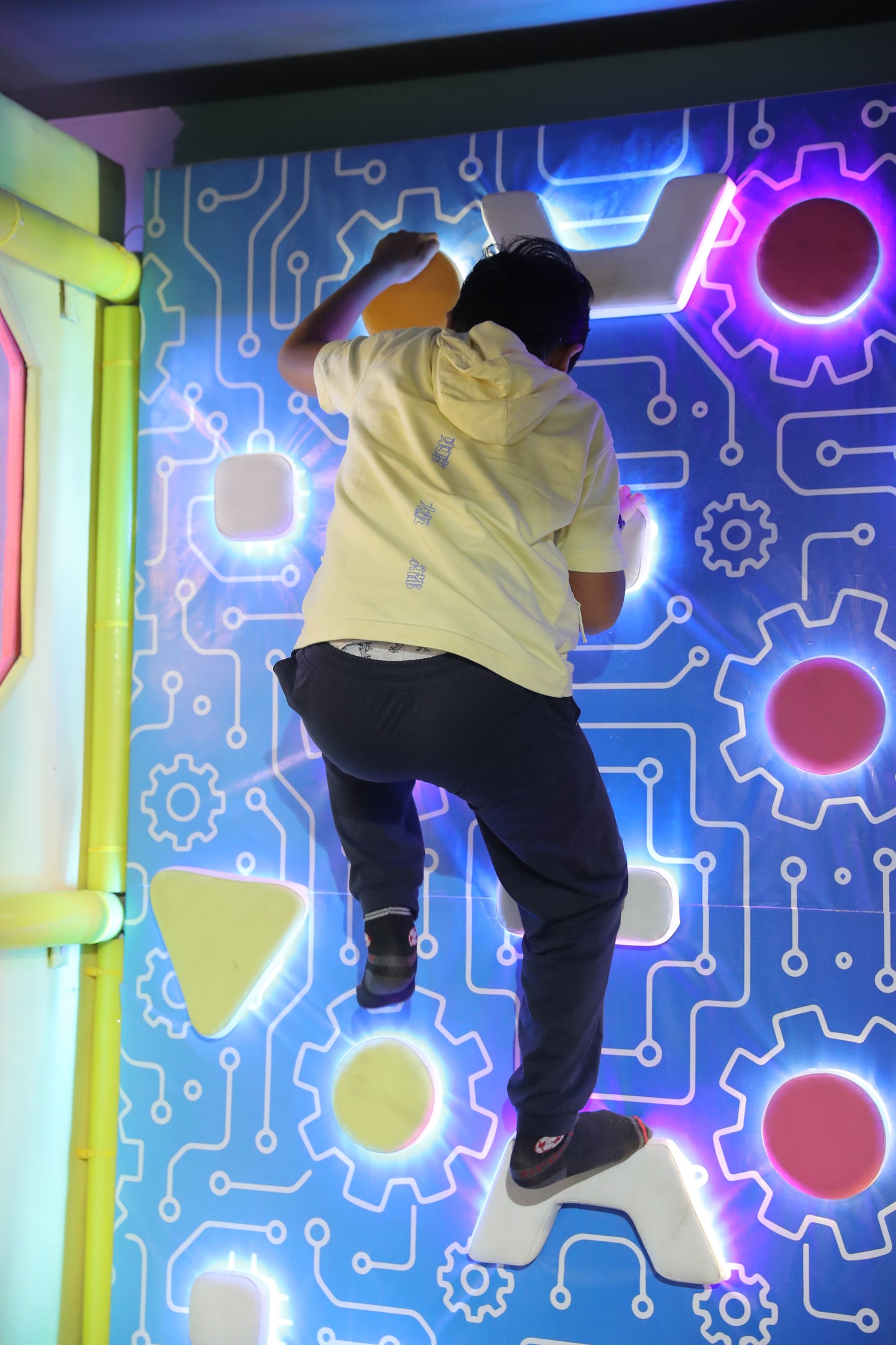 A child climbs a brightly lit wall with a circuit board design.