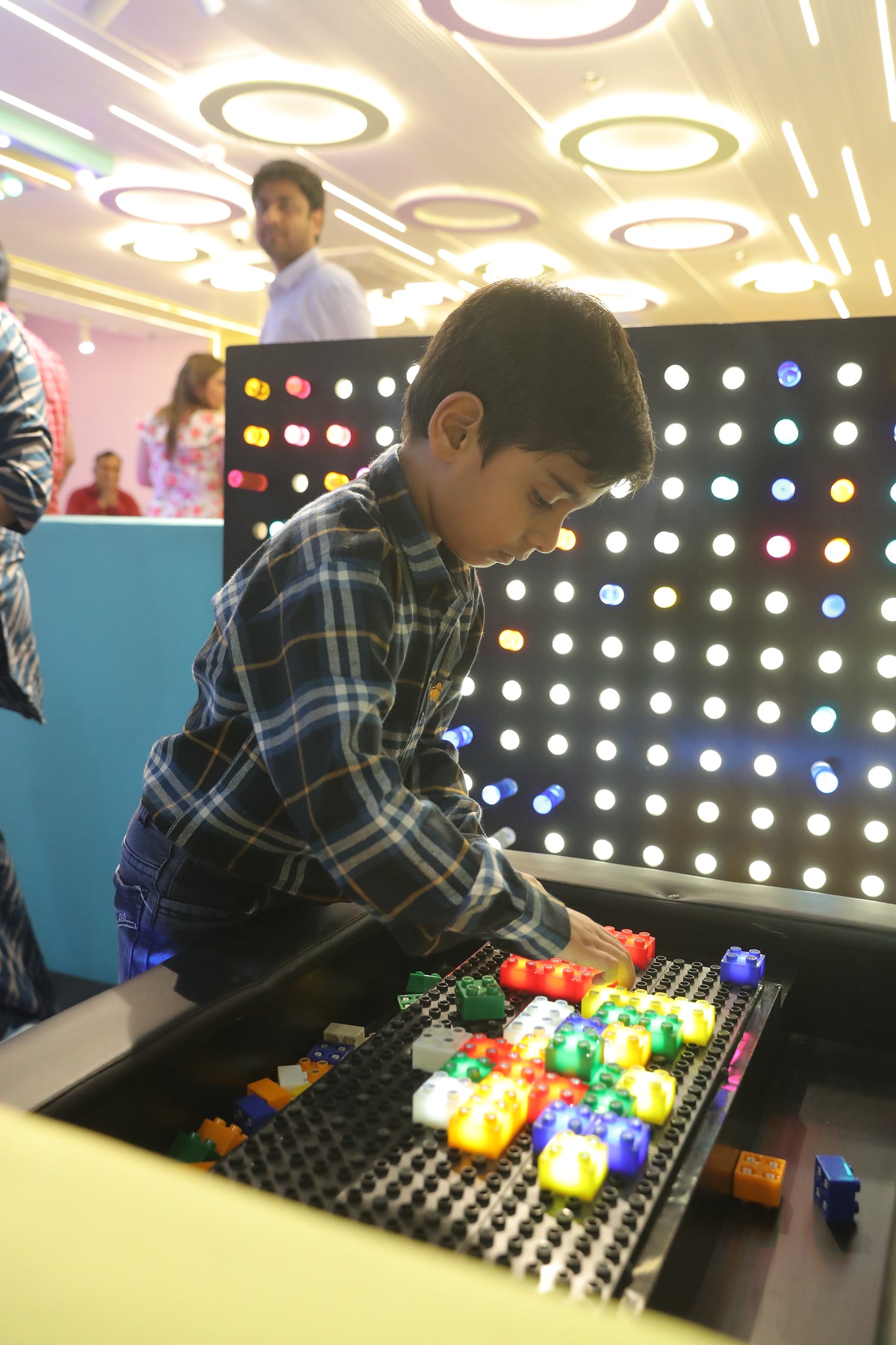 A young boy plays with colorful building blocks in front of a wall of lights.