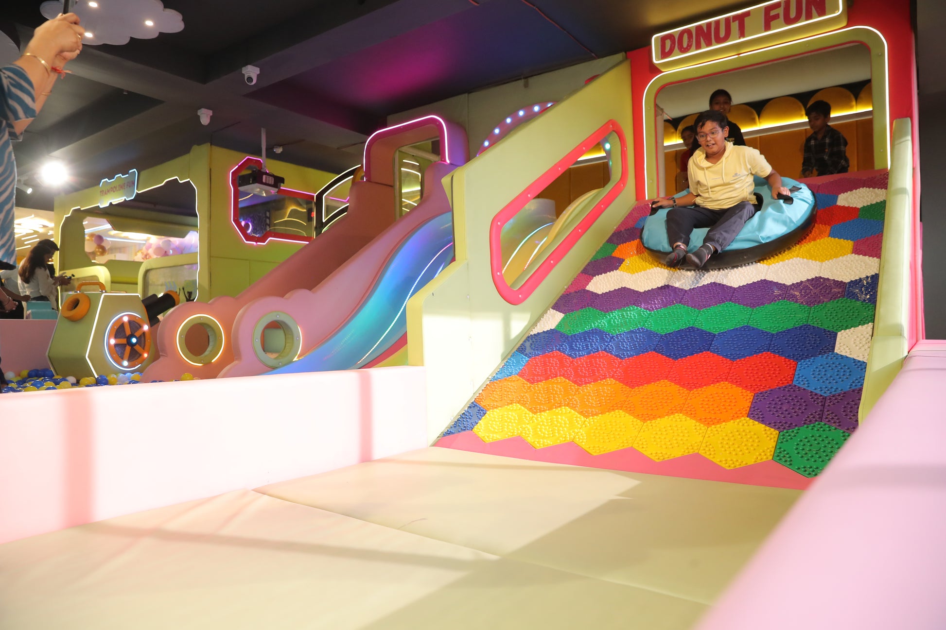 Children slide down a colorful playground slide at an indoor amusement center.