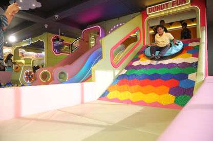 Children slide down a colorful playground slide at an indoor amusement center.