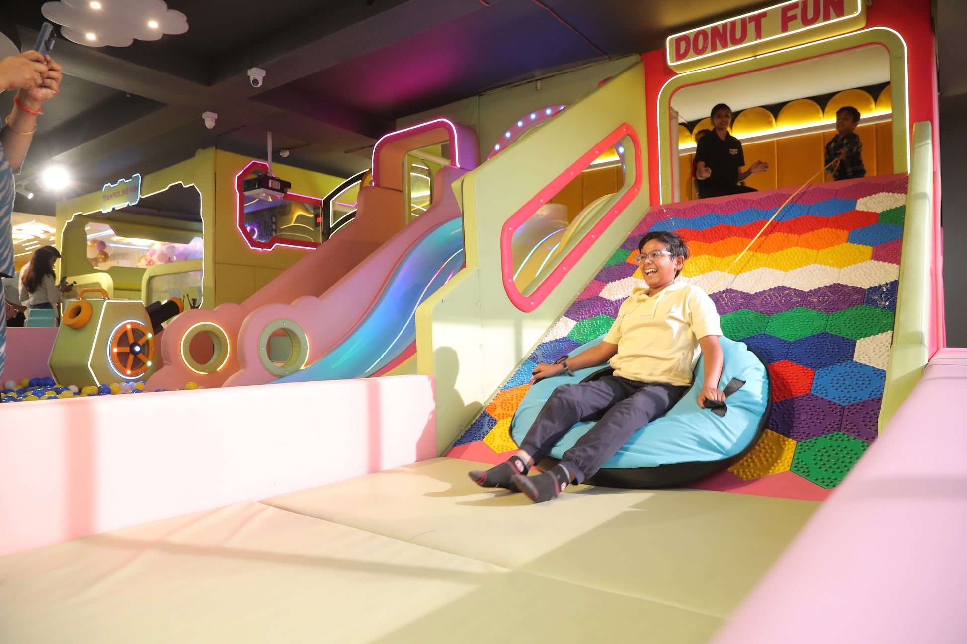 A young boy laughs as he slides down a colorful play structure in an indoor amusement park.