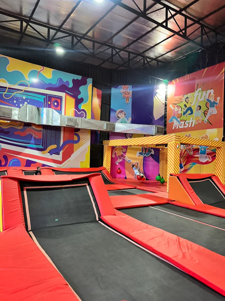 An indoor trampoline park with colorful murals and several trampolines. A child is seen jumping on a trampoline.