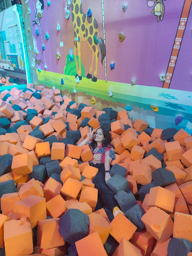 A young woman poses in a foam pit at a trampoline park with a giraffe mural on the wall.