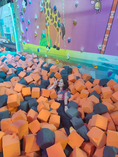 A young woman poses in a foam pit at a trampoline park with a giraffe mural on the wall.