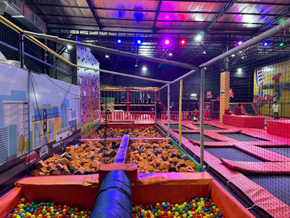 An indoor trampoline park with a foam pit and colorful balls, where children are playing.