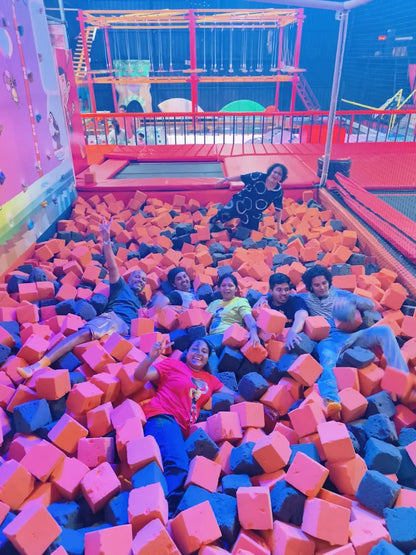A group of young adults joyfully play in a foam pit at an indoor adventure park.