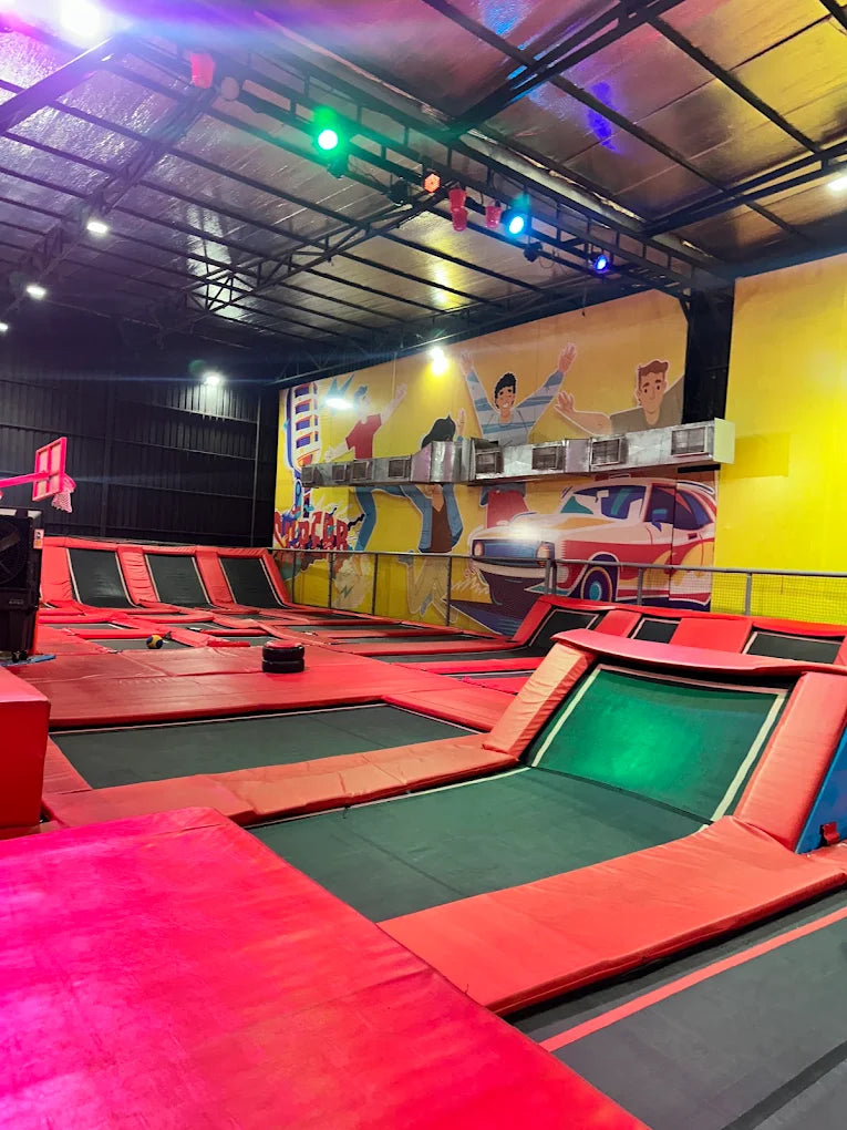 An indoor trampoline park with multiple red and green trampolines, illuminated by colorful lights.