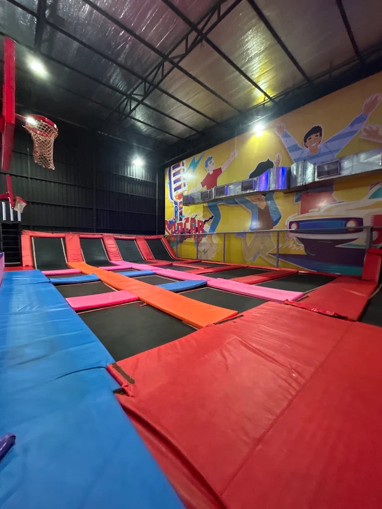 An indoor trampoline park with colorful padded areas and a basketball hoop.