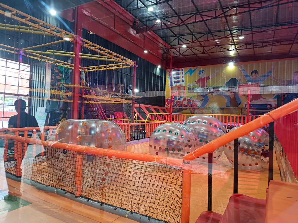 An indoor adventure park with a rope course and inflatable balls, seen from behind a person.