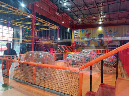 An indoor adventure park with a rope course and inflatable balls, seen from behind a person.