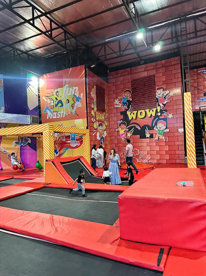 Children and adults enjoy a trampoline park with colorful walls and red padded areas.