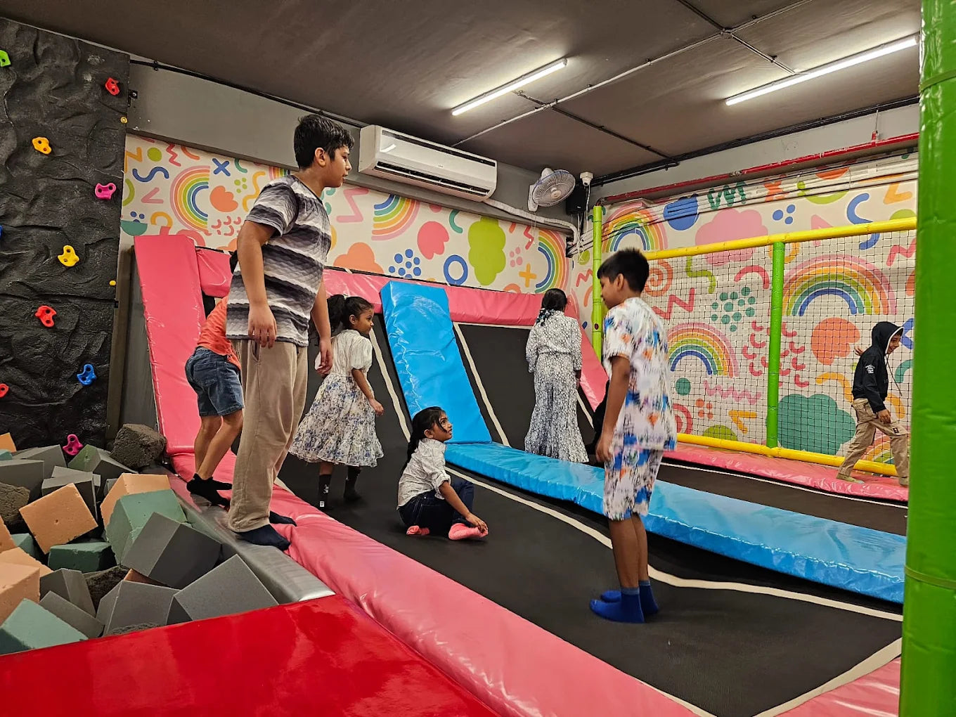 Children play on trampolines and foam pits in a colorful indoor play area.