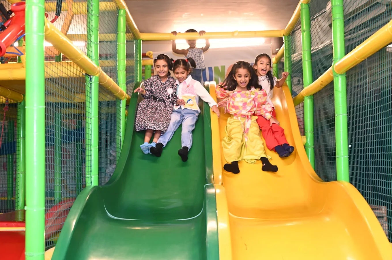 Children slide down colorful playground slides in a soft play area.