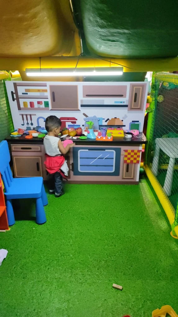 A young child plays in a toy kitchen in a brightly colored indoor play area.