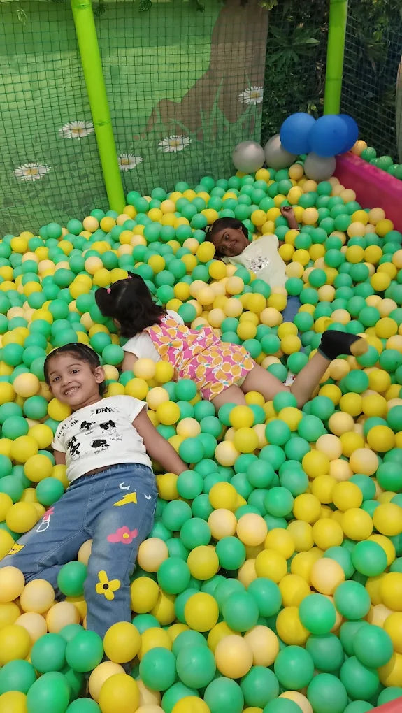 Three young children play in a ball pit filled with green and yellow balls.