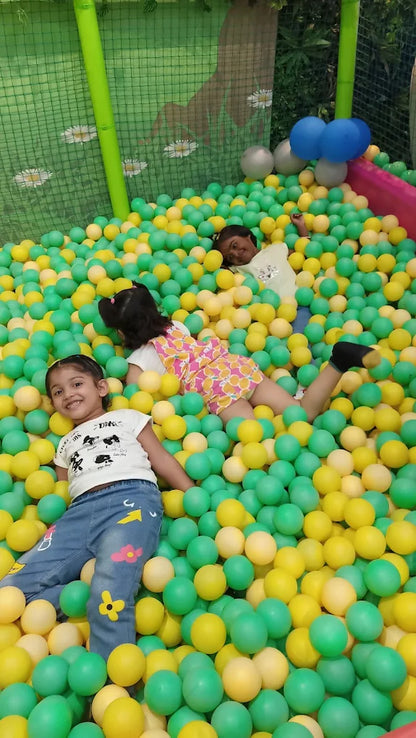 Three young children play in a ball pit filled with green and yellow balls.