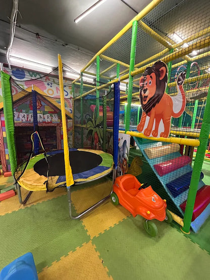 A colorful indoor playground with a trampoline, slide, and toy car for young children.