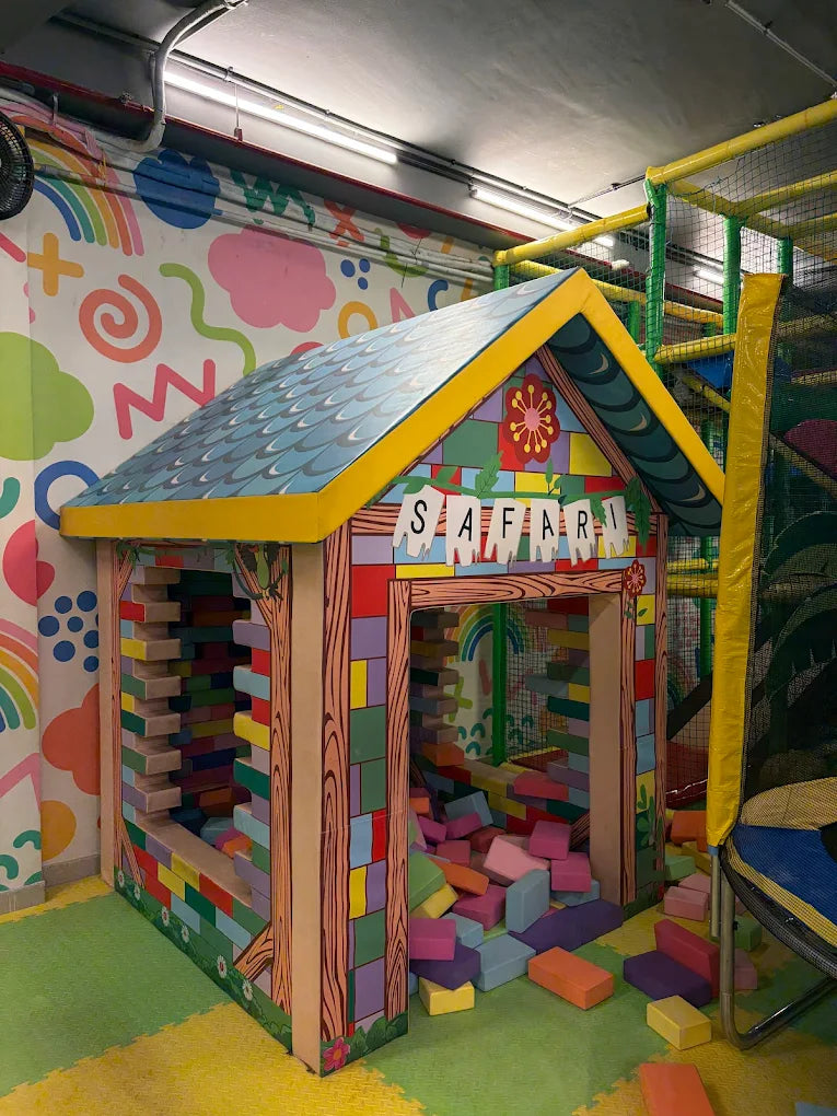 A colorful playhouse with "Safari" written above the entrance, filled with soft blocks, in a children's indoor play area.