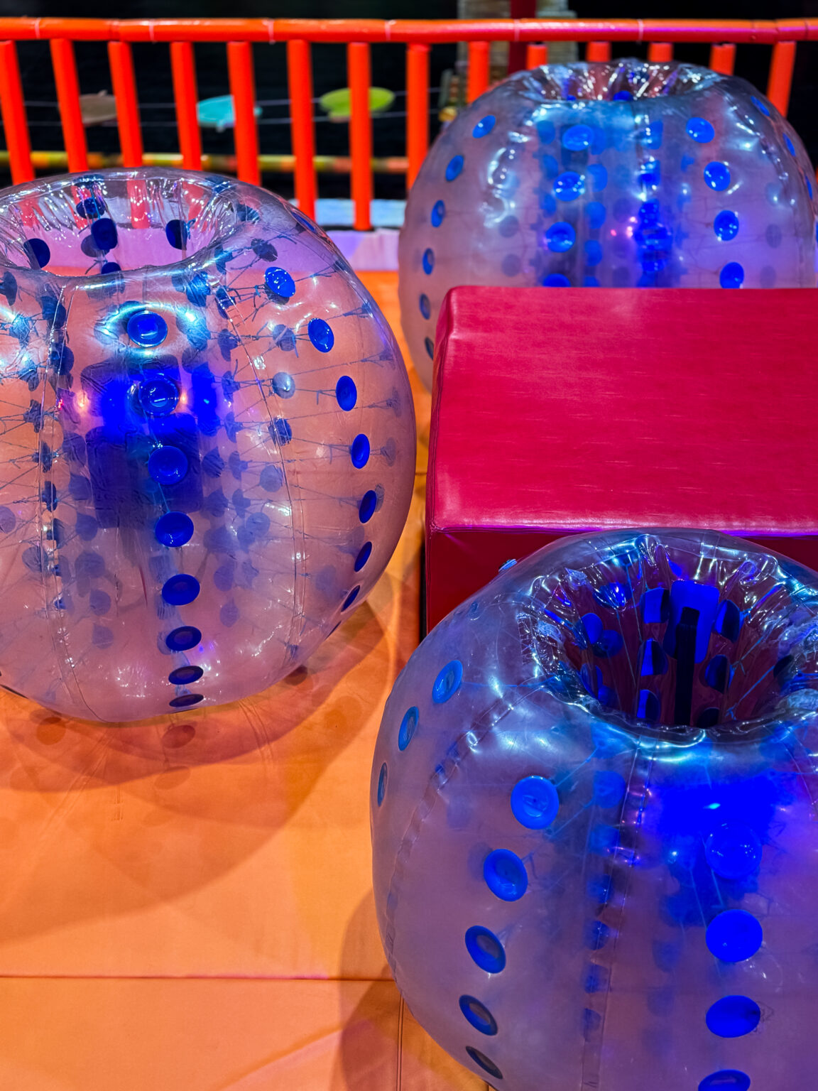 Inflatable bumper balls with blue dots are on an orange surface, with a red barrier in the background.